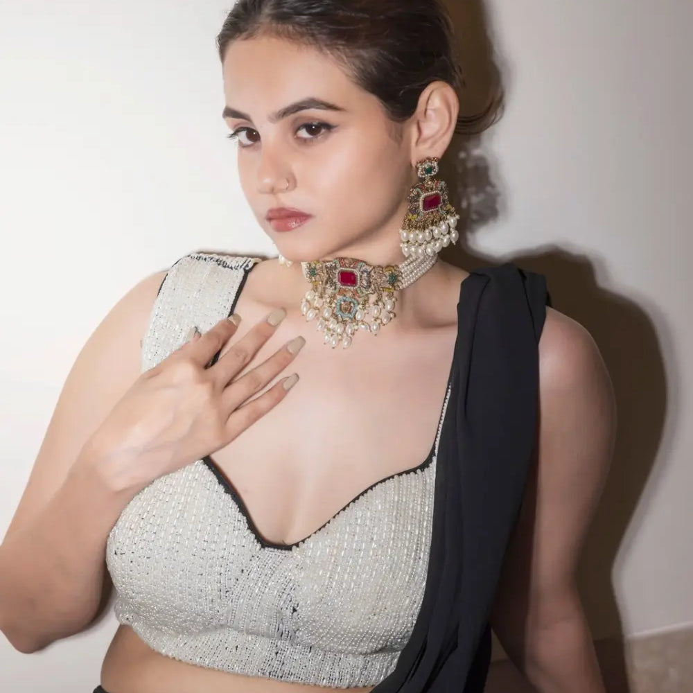 
                      
                        A woman wearing a silver and multicolor jadau choker necklace set with a red ruby center, along with matching earrings.
                      
                    